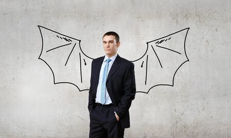 Young businessman with drawn bat wings behind backの写真素材