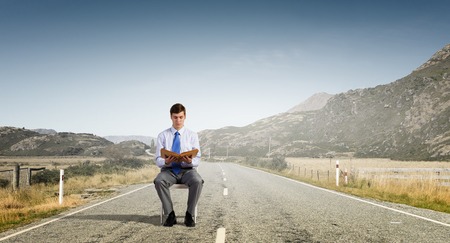 Businessman sitting in chair and reading bookの写真素材
