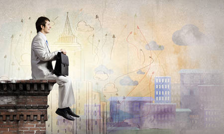 Young businessman with briefcase sitting on top of buildingの写真素材