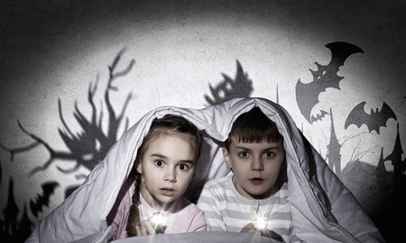 Children sitting in bed under blanket with flashlightsの写真素材