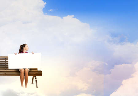 Young woman with white blank banner sitting on benchの写真素材