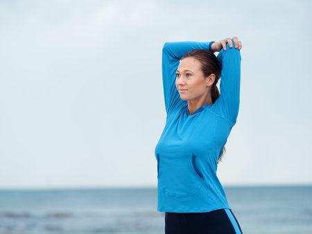 Sporty young woman stretching on the sea coast