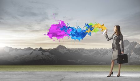 Businesswoman spraying colorful paint splashes from containerの写真素材