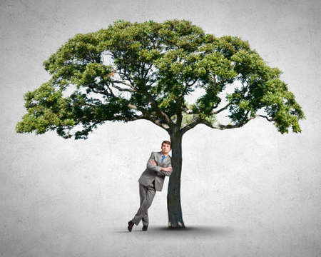 Young relaxed businessman leaning on green treeの写真素材