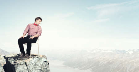 Troubled young man sitting in chair outdoorsの写真素材