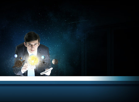 Young businessman looking on table and planets of space spinning around