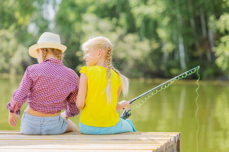 Rear view of two children sitting at bank and fishingの写真素材