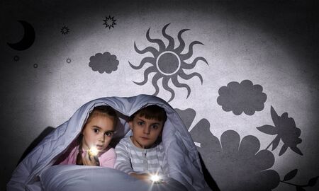 Children sitting in bed under blanket with flashlightsの写真素材