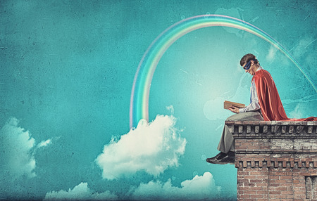 Young man in superhero costume reading bookの写真素材