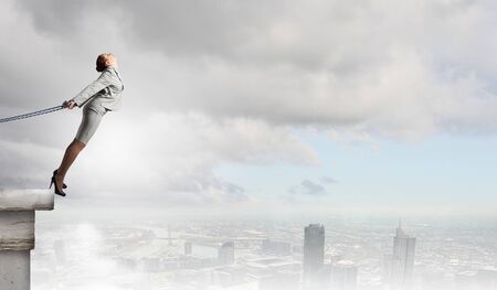 Young businesswoman with ropes on hands trying to flyの写真素材