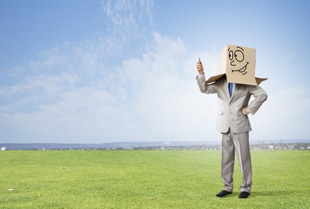 Businessman wearing carton box with drawn emotions on headの写真素材