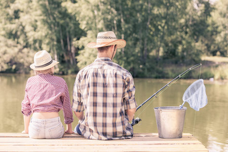 Rear view of father and daughter sitting on bridge and fishing