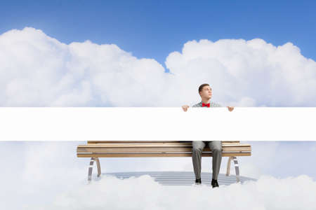 Young man with white blank banner sitting on benchの写真素材