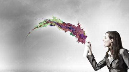 Businesswoman spraying colorful paint splashes from container