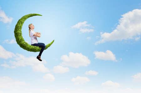 Young girl sitting on green moon high in skyの写真素材