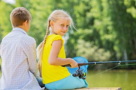 Rear view of two children sitting at bank and fishingの写真素材