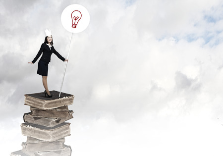 Young businesswoman in paper crown standing on pile of booksの写真素材