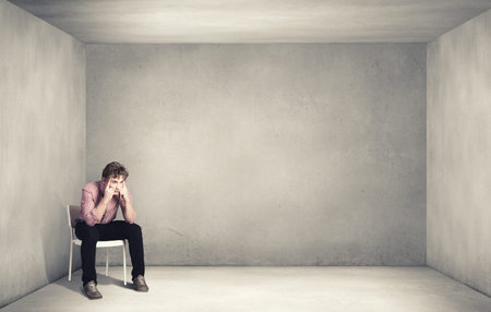Troubled young man sitting in chair outdoorsの写真素材