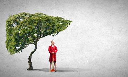 Blond woman in red coat with axe and green treeの写真素材