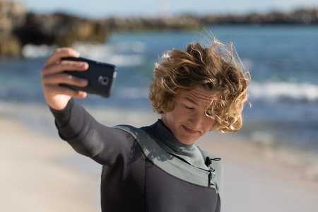 A surfer with his surfboard at the beach doing selfieの写真素材