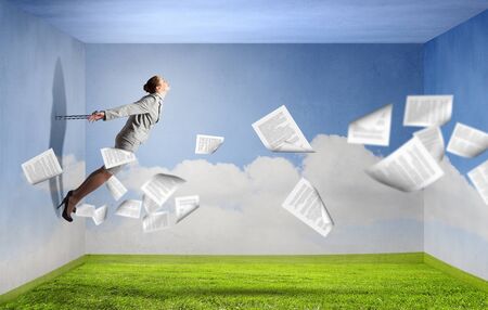 Young businesswoman with ropes on hands trying to flyの写真素材