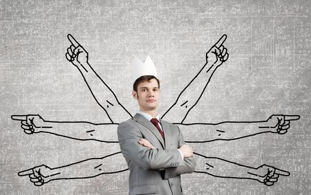 Young businessman in paper crown and many hands around himの写真素材