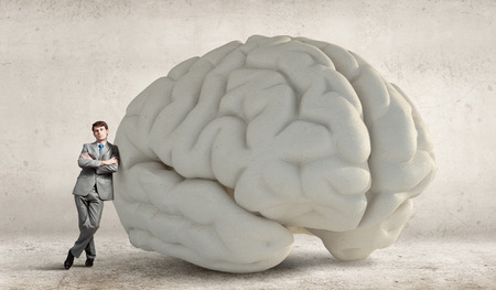 Confident businessman leaning on huge human brainの写真素材