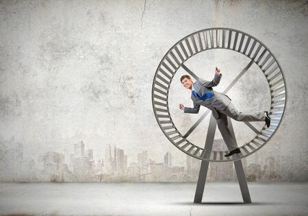 Young businessman running in huge hamster wheelの写真素材
