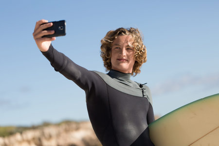 A surfer with his surfboard at the beach doing selfie
