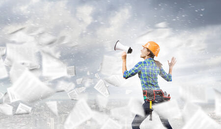 Young woman builder screaming emotionally in megaphoneの写真素材