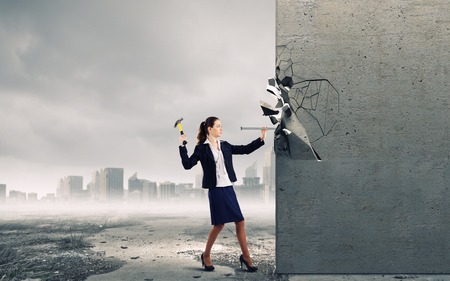 Young businesswoman hitting nail in wall with hammerの写真素材
