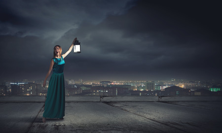 Young woman in green dress with lantern in darknessの写真素材