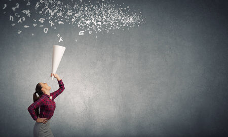 Young pretty woman screaming in paper trumpetの写真素材