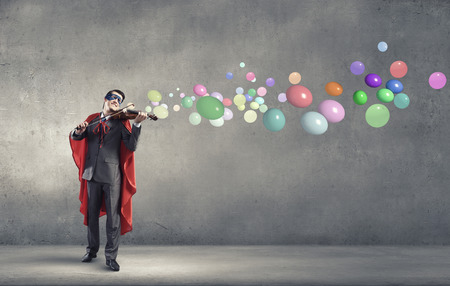 Young man in superhero costume playing violinの写真素材