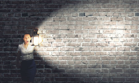 Young businesswoman walking in darkness with lantern in handの写真素材