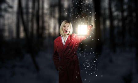 Young blonde in red cloak with lantern in night forestの写真素材