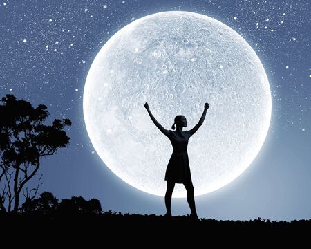 Silhouette of woman against full moon with hands upの写真素材