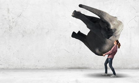 Young girl making effort to carry huge elephantの写真素材
