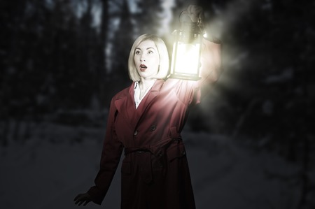 Young blonde in red cloak with lantern in night forestの写真素材