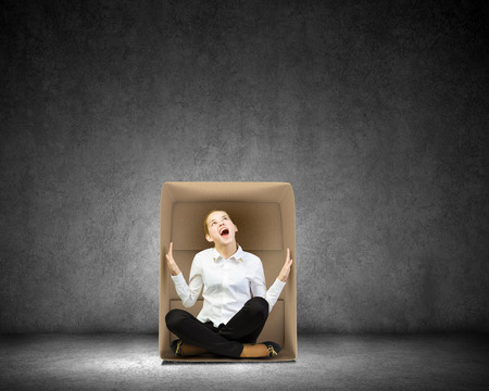 Young businesswoman sitting in carton box and feeling uncomfortableの写真素材
