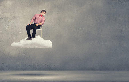 Troubled young man sitting in chair on cloudの写真素材