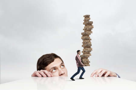 Young businessman looking from under table at man carrying pile of booksの写真素材