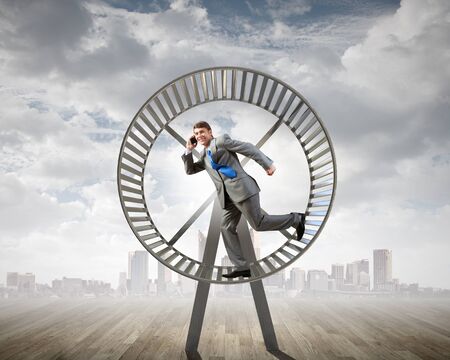 Young businessman running in huge hamster wheelの写真素材