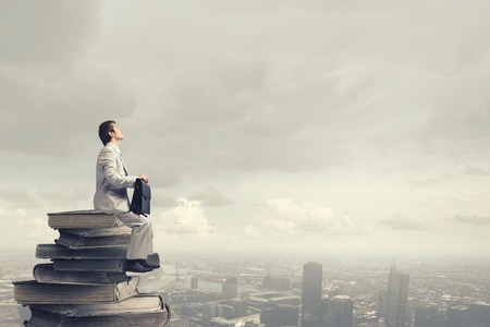 Young man sitting on pile of old booksの写真素材