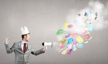 Young businessman in paper crown screaming in megaphoneの写真素材