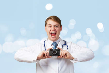 Funny young doctor with photo camera screaming emotionallyの写真素材