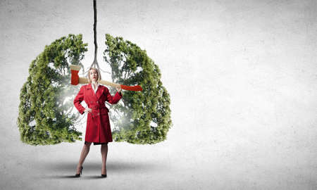 Blond woman in red coat with axe and green treeの写真素材