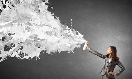 Businesswoman spraying white paint splashes from containerの写真素材