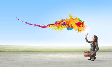 Businesswoman spraying colorful paint splashes from containerの写真素材