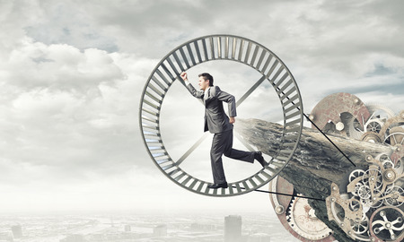 Young businessman in suit running in hamster wheelの写真素材
